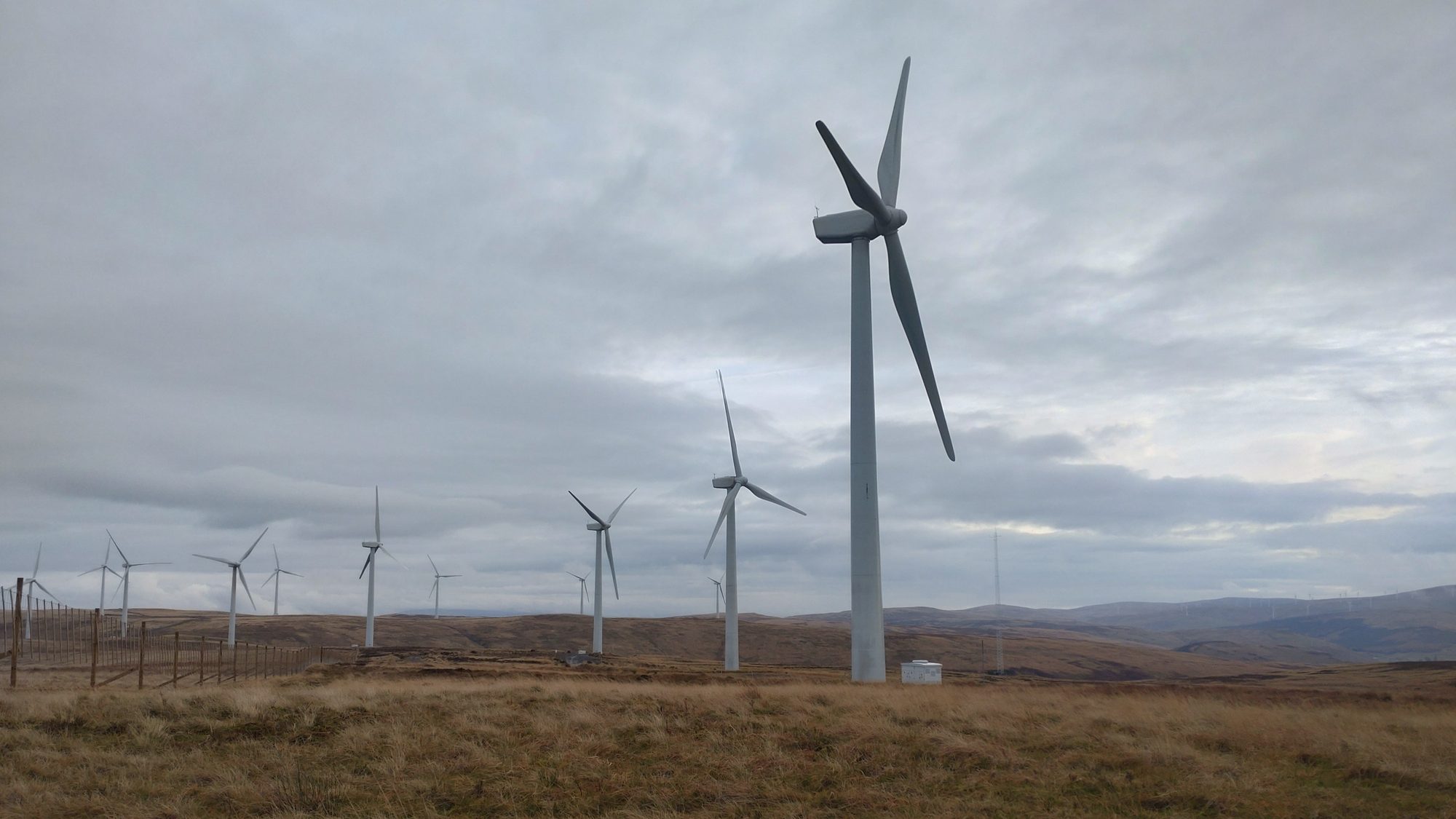 Onshore wind farm on open moorland under a grey sky, a large turbine in the foreground