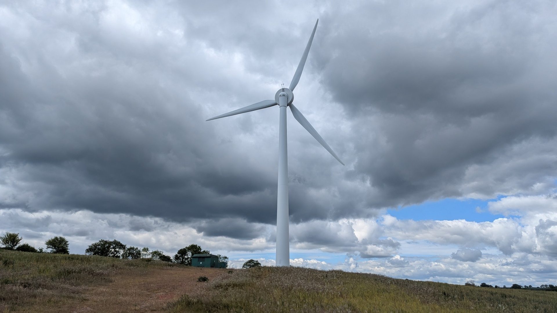 Single wind turbine on a grassy hilltop under a heavy sky