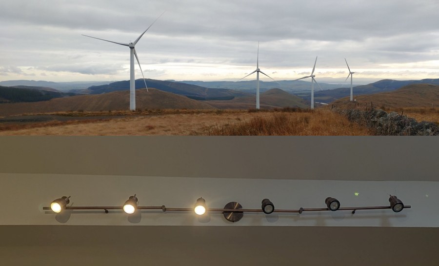 Above, a row of wind turbines on a Scottish hillside under grey cloud. Below, a kitchen ceiling light bar where three of seven bulbs are lit and four have failed.